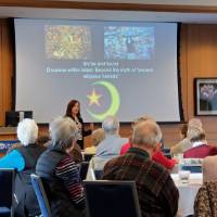 A woman speaks to a group of people in front of a presentation displaying pictures of Muslims